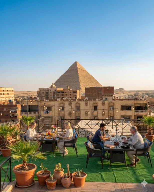 a group of people sitting at tables with the pyramid in the background at Families Pyramids view - Rooftop in Cairo