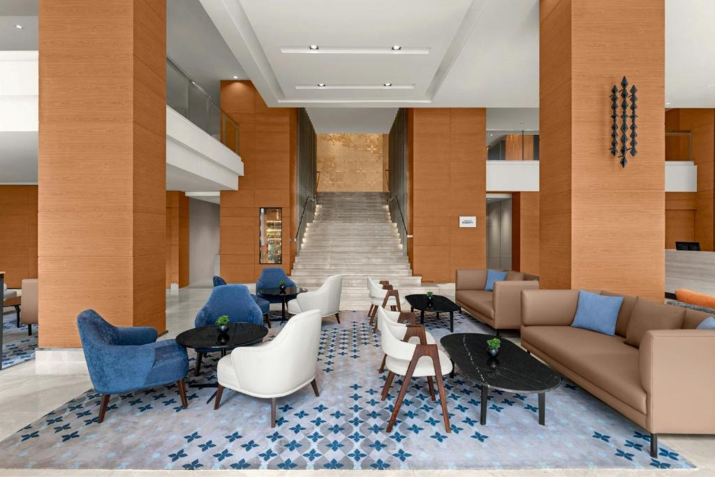 A spacious lobby lounge with sofas, armchairs, tables, and a prominent staircase.