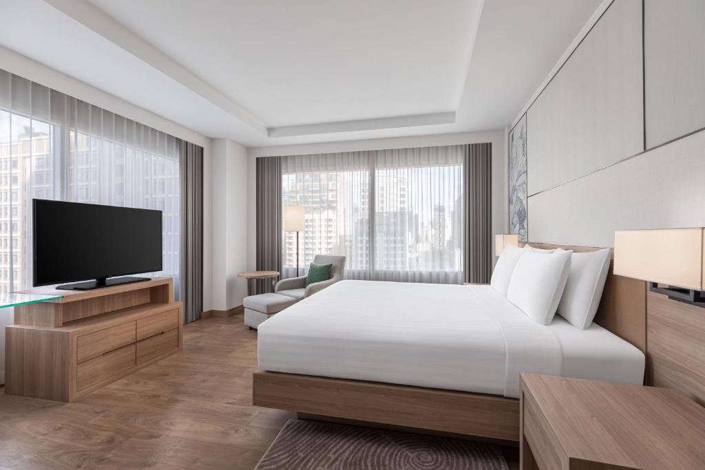 A king-bed room with a television, lounge chair and broad city-facing windows.