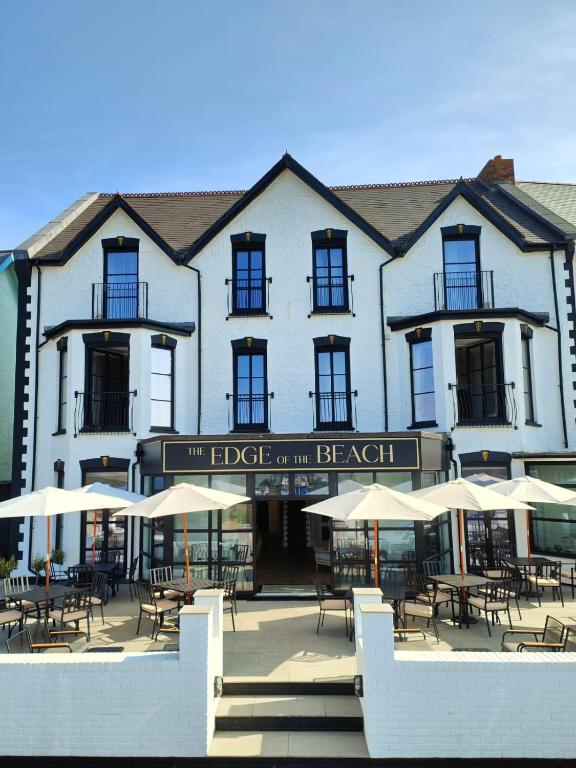 a large white building with tables and chairs and umbrellas at The Edge Of The Beach in Bude