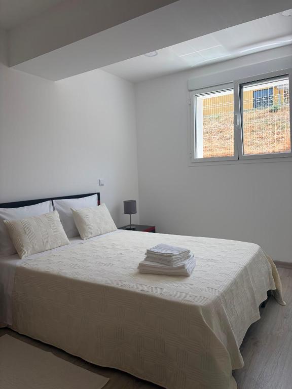 a white bedroom with a large bed with two windows at Alojamento das cantarinhas in Bragança