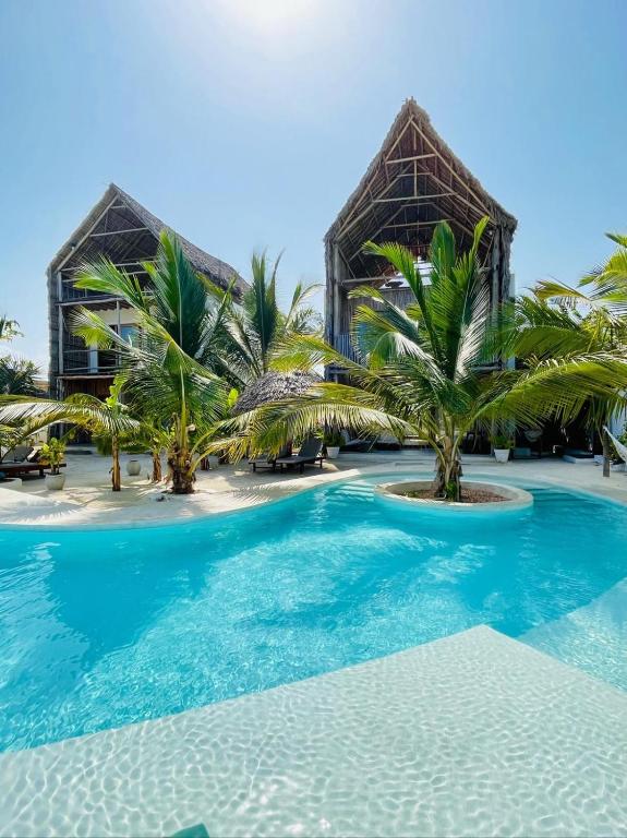 a swimming pool in front of a building with palm trees at Mfumbwi Twins Villa in Jambiani