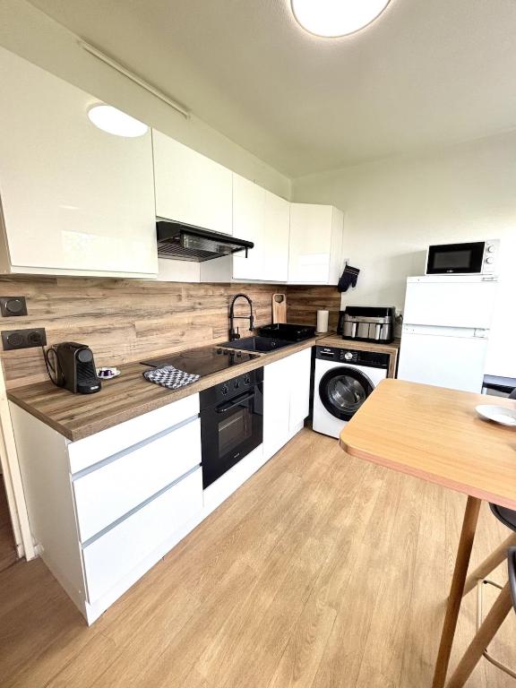 a kitchen with white cabinets and a wooden floor at Bricks Pérignon - Tram, lit Queen size & air fryer in Chenôve