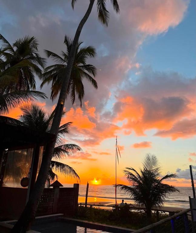 a sunset on a beach with palm trees and the ocean at Club Manguaba Beira Mar in Japaratinga