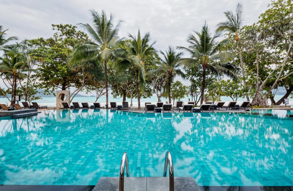 a large swimming pool with palm trees and chairs at Impiana Beach Front Resort Patong, Phuket in Patong Beach