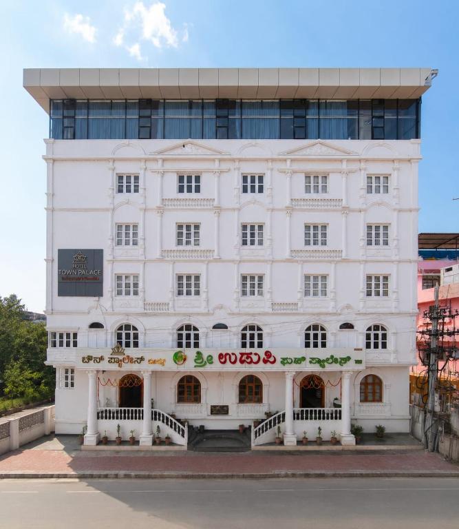 a white building in front of a tall building at Hotel Town Palace in Shimoga