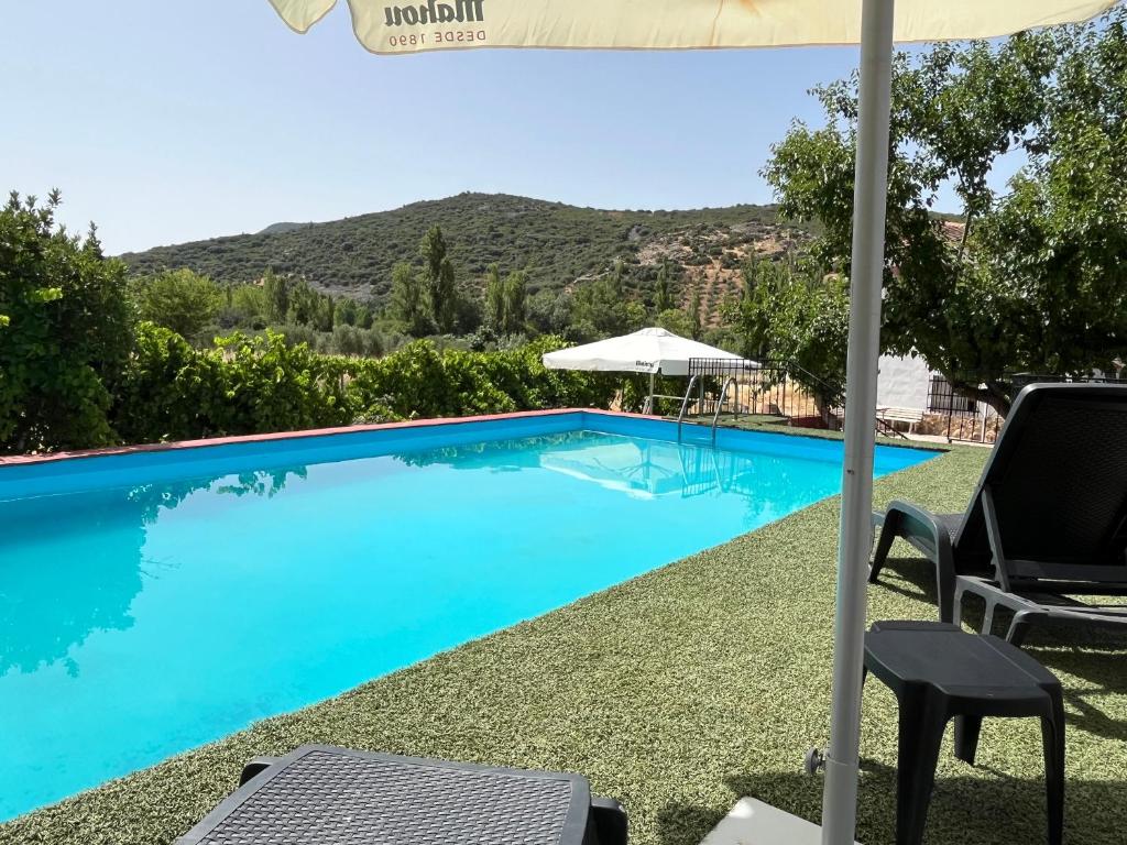 a blue swimming pool with chairs and an umbrella at Casa Rural Angorrilla in Reolid
