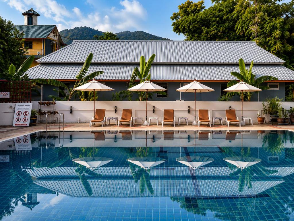 a pool with chairs and umbrellas in front of a building at Rabbit Mansion Patong Hotel in Patong Beach