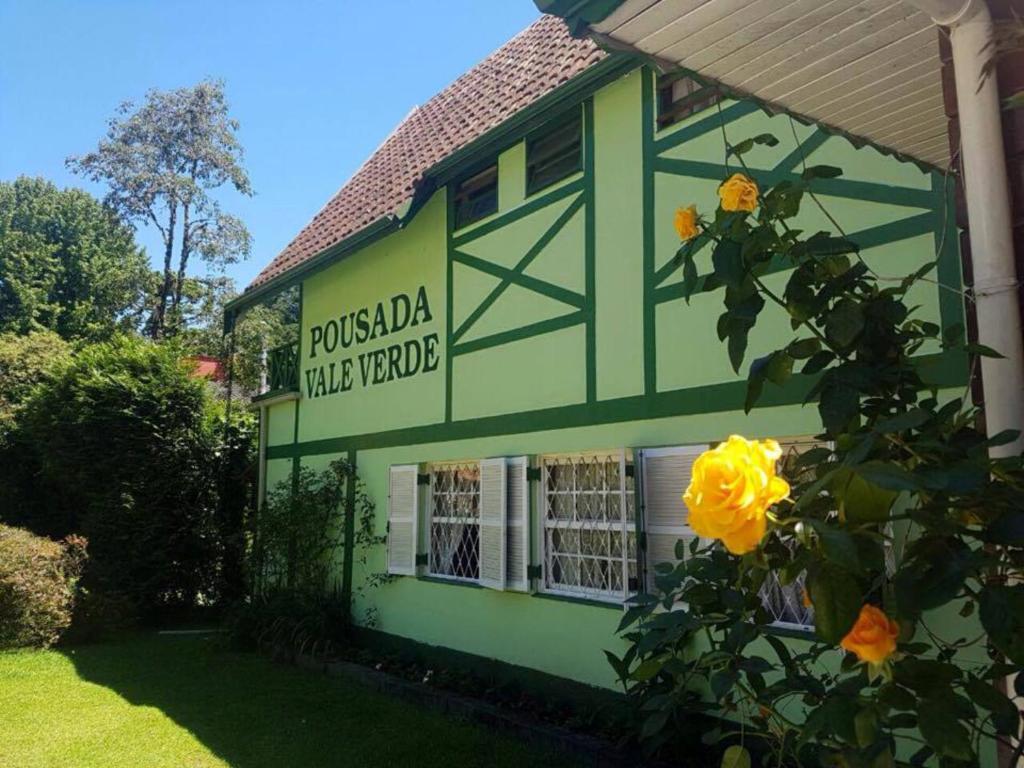 un edificio verde con una rosa amarilla delante de él en Pousada Vale Verde, en Campos do Jordão