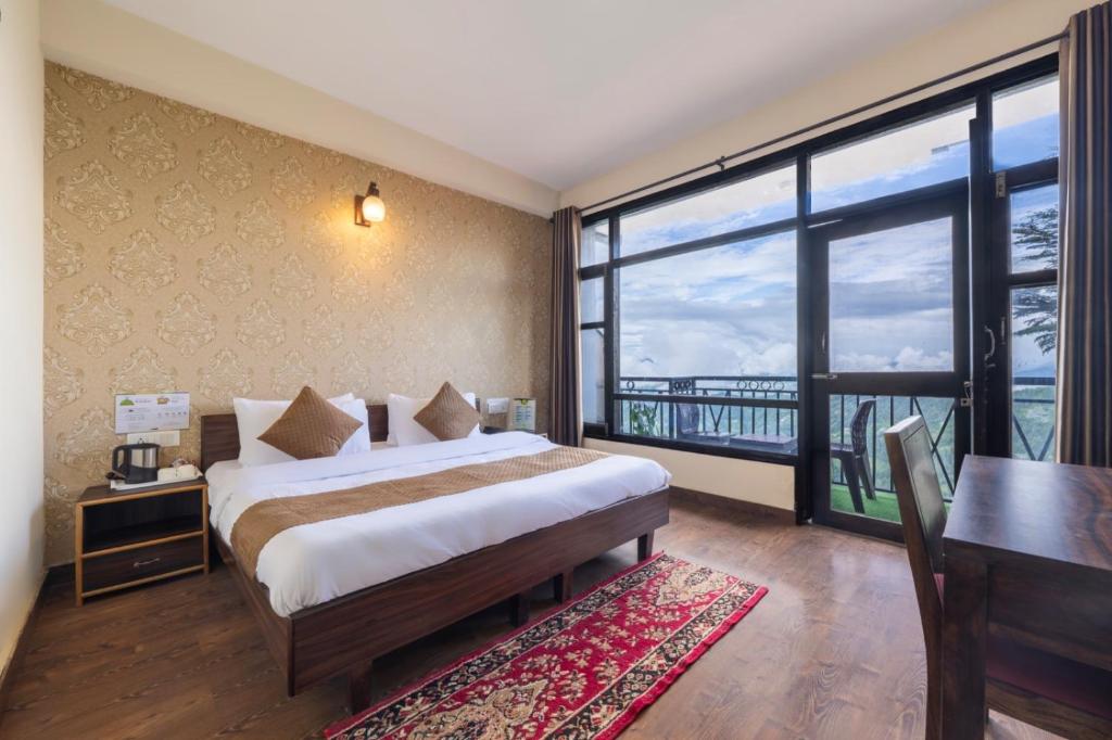 a bedroom with a bed and a desk and a large window at AyurVeda Haven Shimla l Pure Veg l l Lift l Power Backup l Multi Cuisine Restaurant l Free Parking l By Exotic Stays in Kūfrī