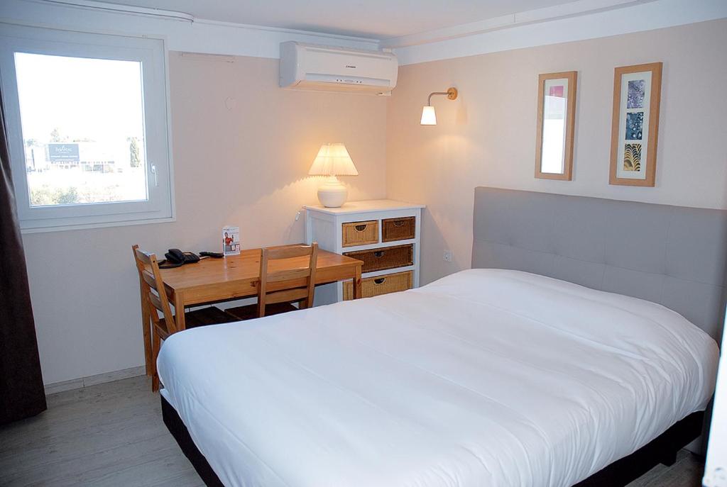 - une chambre avec un lit blanc et un bureau avec une lampe dans l'établissement Contact Hotel LE SUD Montpellier Aéroport Parc Expo Arena, à Mauguio