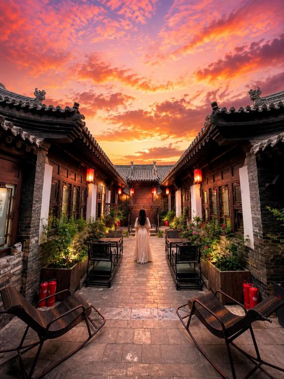 a woman in a white dress walking down a courtyard at sunset at Elsewhere Hotel Inn Ancient City Center Branch in Pingyao
