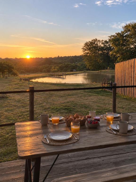 a wooden table with food on it with the sunset at Cocolac- gîte avec étang privé en Corrèze- in Lubersac