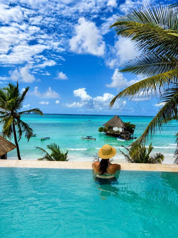 a woman in a hat sitting in a swimming pool looking at the ocean at Villa Duara Zanzibar Rooftop Infinity Pool The Rock View in Michamvi