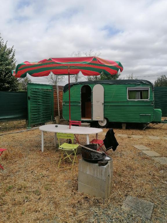 a table with an umbrella next to a trailer at Caravane au bord de la rivière in Saint-Corneille