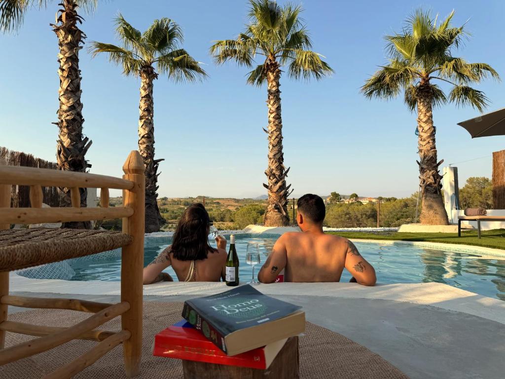 a man and a woman sitting next to a swimming pool with palm trees at Peralta Villas Boutique Adults Only in Renau