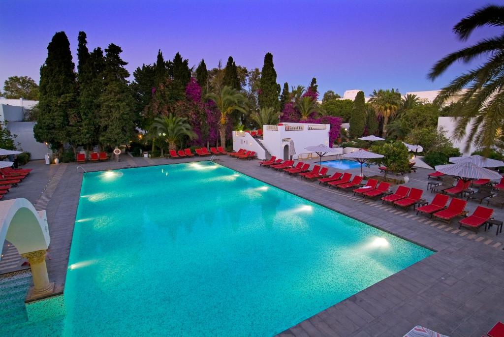 une grande piscine avec des chaises rouges et des parasols dans l'établissement The Orangers Beach Resort and Bungalows All Inclusive, à Hammamet