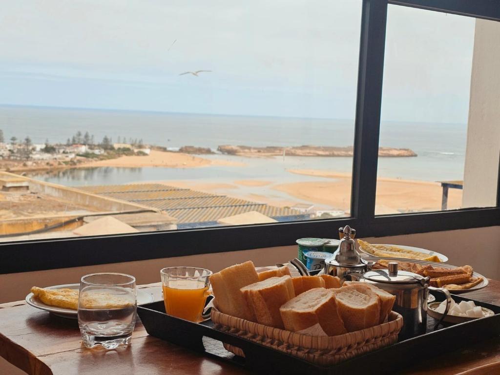 a tray of bread and orange juice on a table with a window at Appartement LE SABLE Uniquement les familles in Oualidia