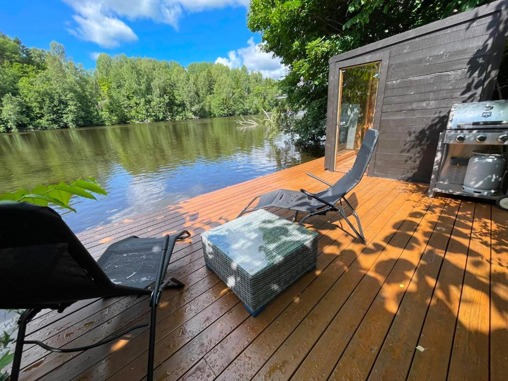 a deck with two chairs and a cooler on the water at Mysigt stuga med bastu in Edsvalla