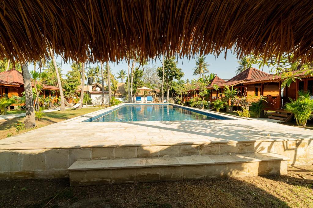a swimming pool in a resort with a straw roof at Welly Bungalow in Gili Trawangan