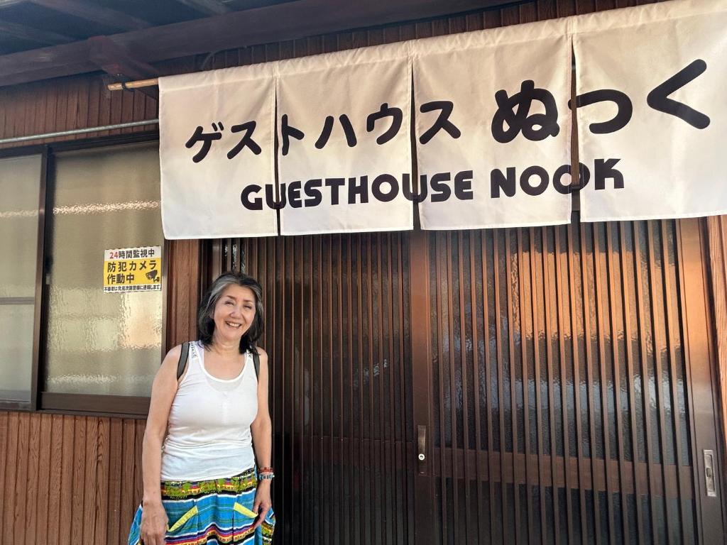 a woman standing in front of a building with a sign at ゲストハウスぬっく in Tanabe