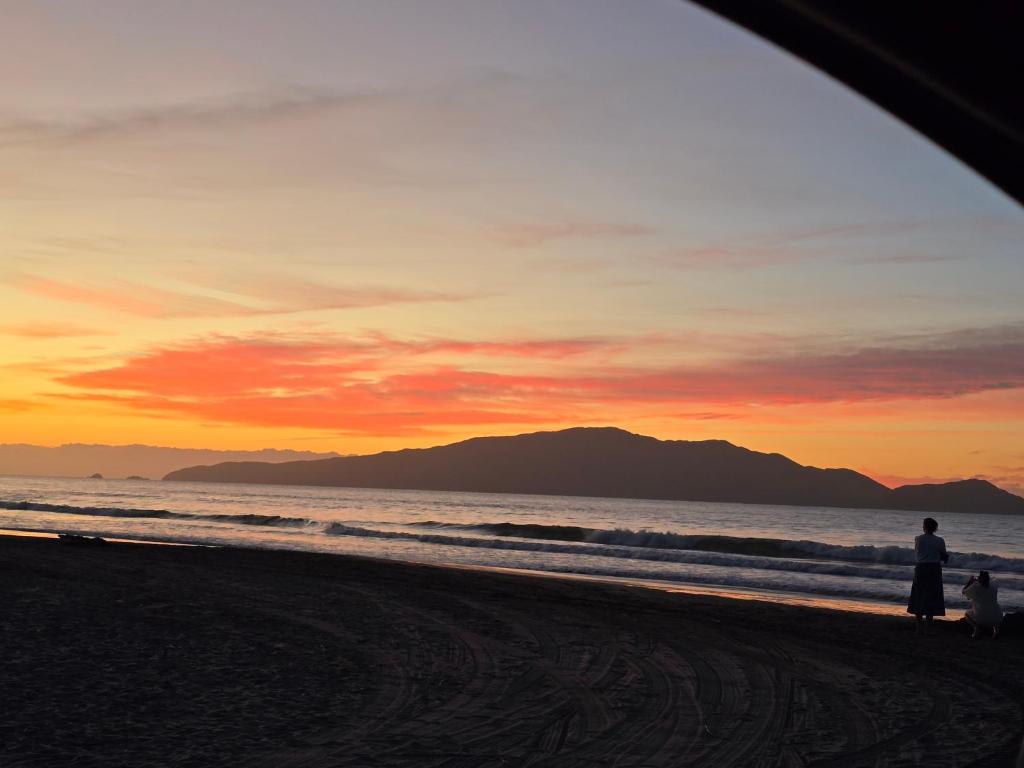 a group of people standing on the beach at sunset at Affordable pit stop Te Horo Beach in Te Horo