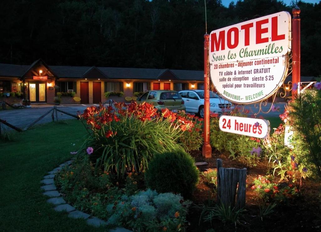 a motel sign in front of a yard with flowers at Motel Sous Les Charmilles in Cap-Santé