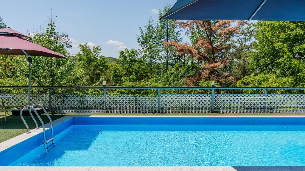 a blue swimming pool with an umbrella next to a fence at Chuncheon Happysday Pet-Friendly Pension in Chuncheon