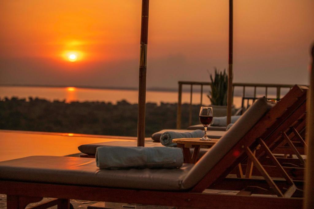 a table with a glass of wine and a sunset at Acacia Wilderness Mweya in Kasese