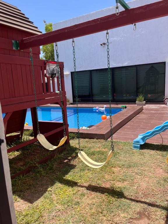a swing in a yard next to a pool at Casa completa, 4 dormitorios, 7 camas dobles, 4 sofá cama, 3 baños 1 en planta baja, cocina equipada, consola Arcade, asador, juguetes para niños, plancha, secadora, cafetera, etc, fraccionamiento privado, zona de vías rápidas y toallas in Torreón
