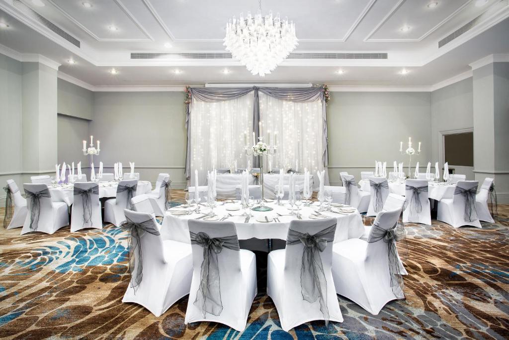 a ballroom with white tables and chairs and a chandelier at Leonardo Royal Hotel Brighton Waterfront in Brighton & Hove