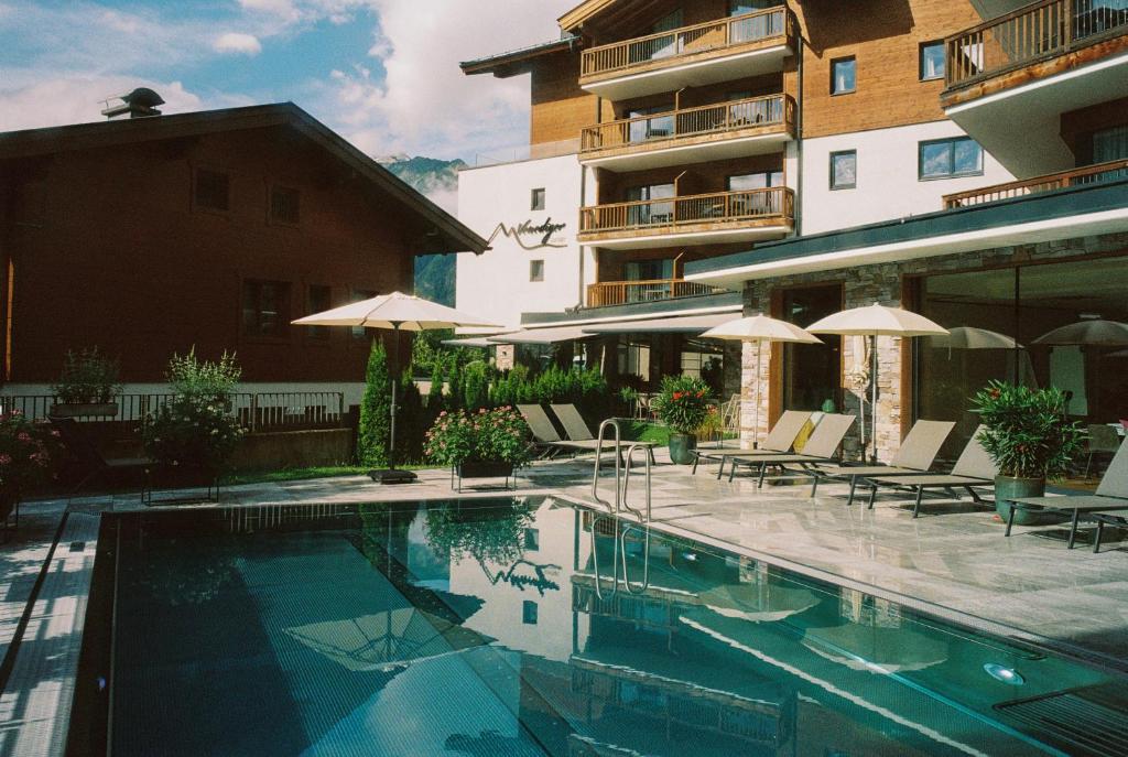 a swimming pool with chairs and umbrellas next to a building at Venediger Lodge in Neukirchen am Großvenediger
