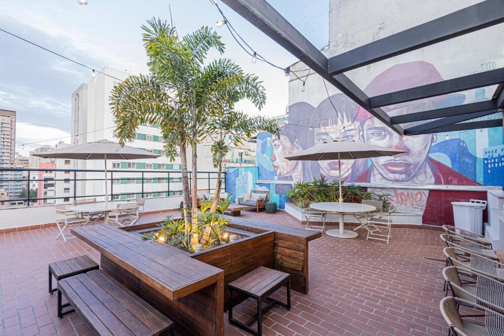 a rooftop patio with benches and tables and a mural at One House by Anora Spaces in São Paulo