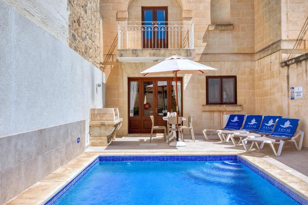 a pool with chairs and an umbrella next to a building at Ta' Gianni in Xewkija