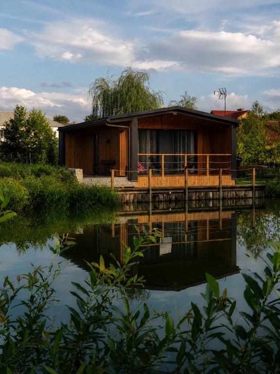 a house on a dock next to a body of water at Roztoczański Domek nad Stawem z jacuzzi in Nowiny