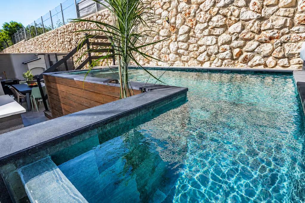 a pool with a palm tree next to a stone wall at אחוזת אבישג - וילה יוקרתית עם בריכה מחוממת וממ"ד למשפחות in Shelomi