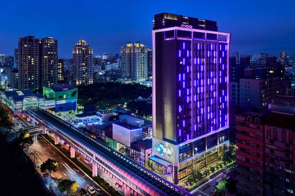 a tall building with purple lights on it in a city at Moxy Taichung in Taichung