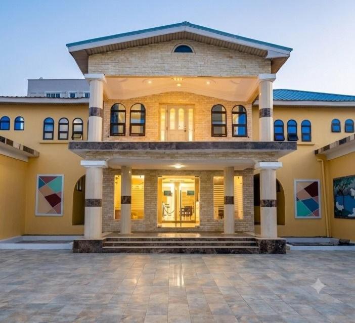a large yellow building with columns and a porch at Adonai Hotel & Apartment in Spintex
