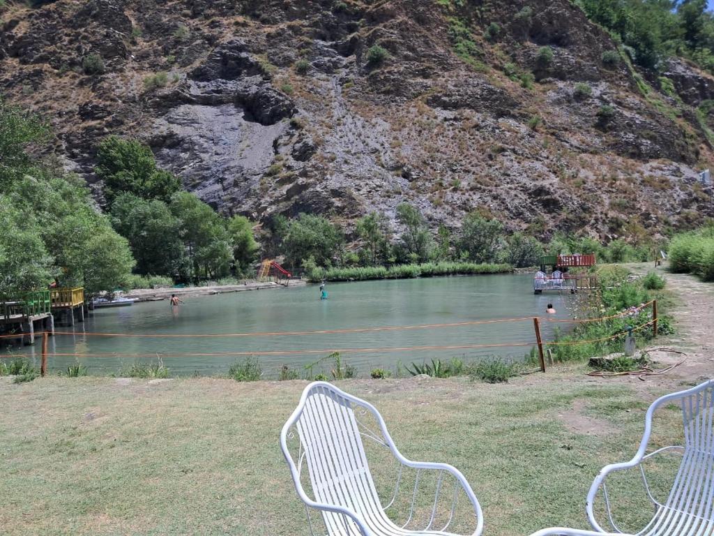 two white chairs sitting in the grass next to a river at Fish Lake Park Guest House in Chitral
