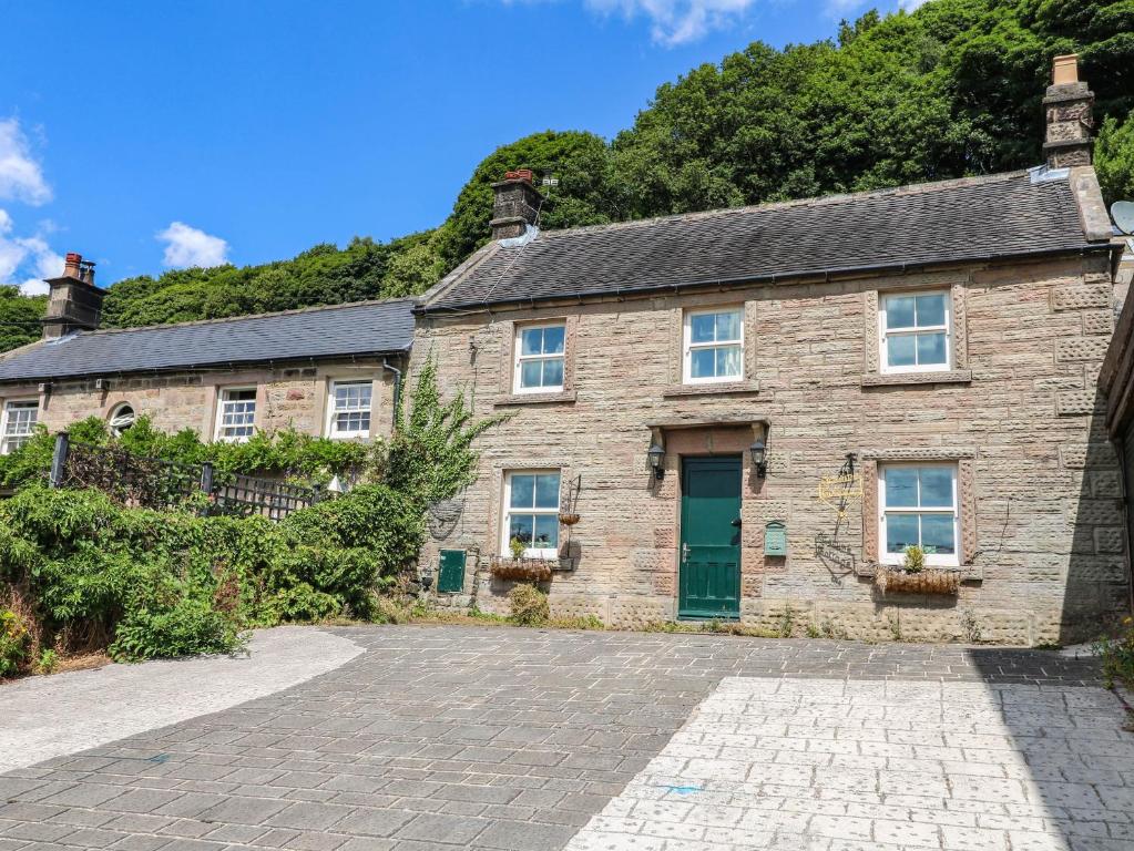 a stone house with a green door and a driveway at Jasmine Cottage in Matlock