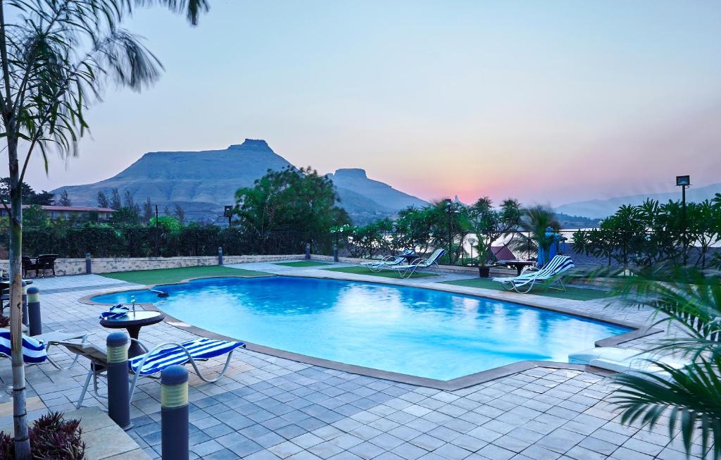 a swimming pool with chairs and mountains in the background at Savana Lake Resort in Nashik