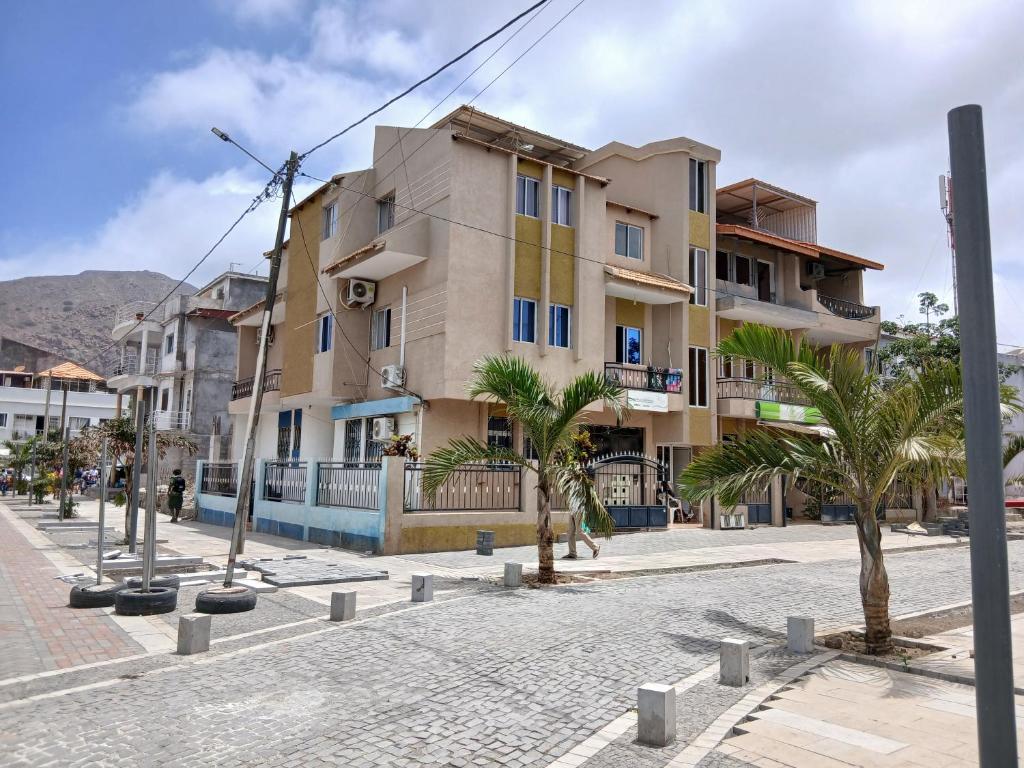 a building on a street with palm trees in front at Apartamento T2-Dunas Centro in Tarrafal