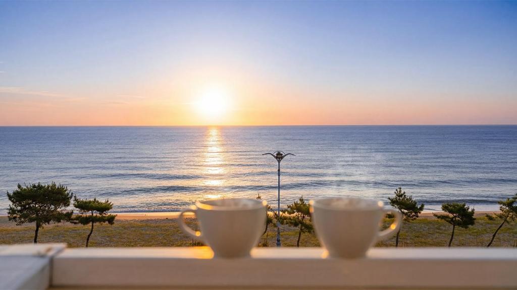 two cups of coffee sitting on a ledge overlooking the ocean at Yangyang Bono Pet-friendly Pension in Yangyang