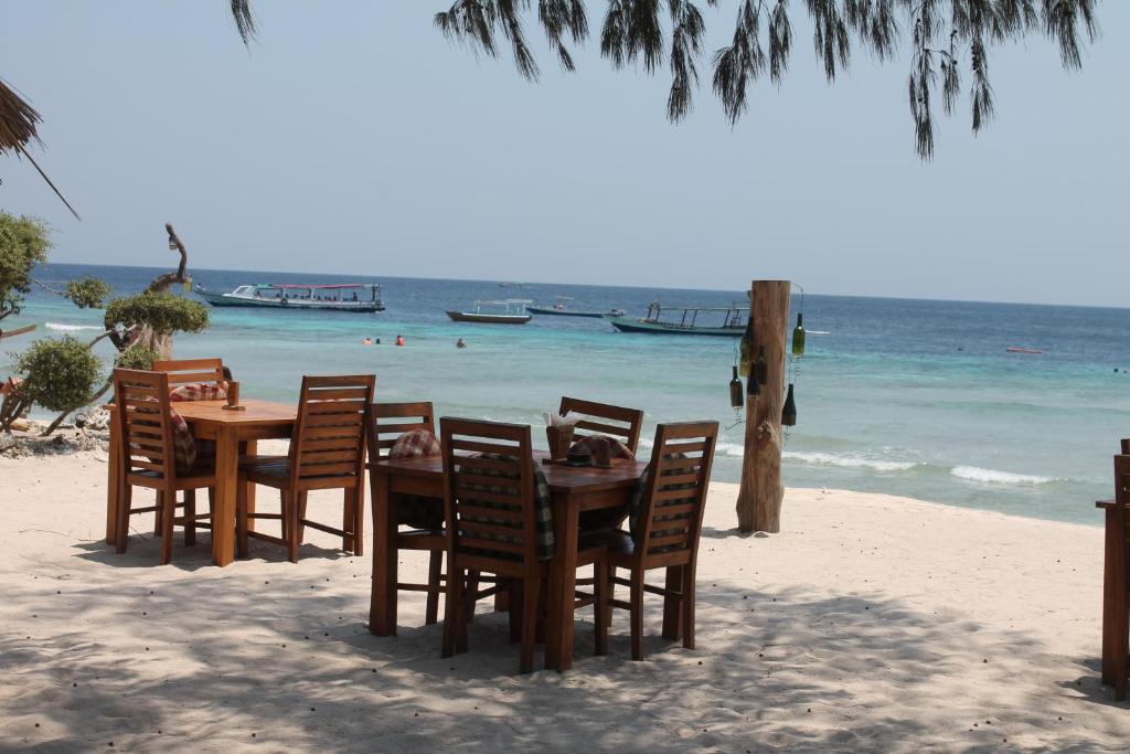una mesa y sillas en una playa con el océano en Melati Cottage, en Gili Trawangan