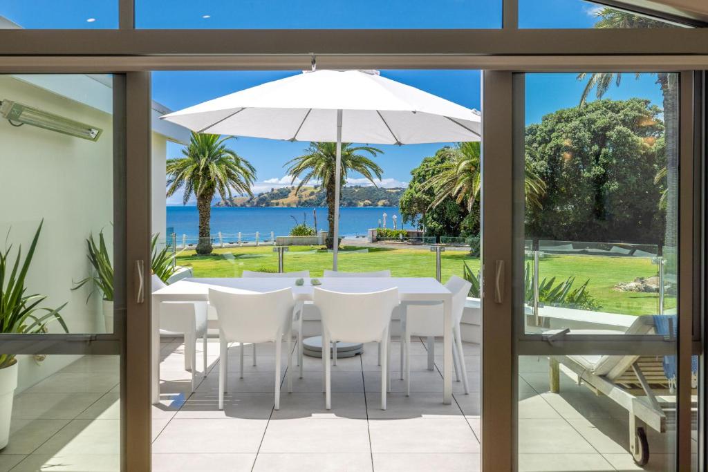 a table with white chairs and an umbrella on a patio at Beachfront 25 The Strand Moana in Waiheke Island
