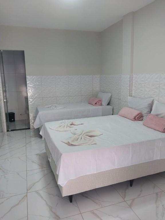 two beds in a white room with pink pillows at Pousada Triângulo in Juazeiro do Norte