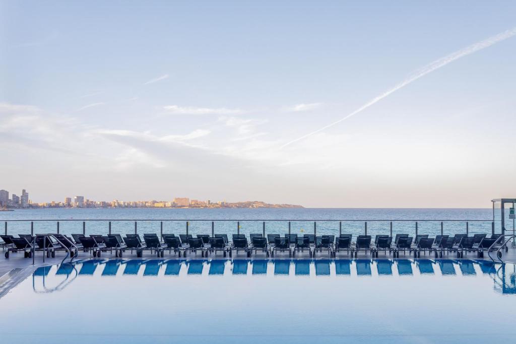 a pool with chairs and the ocean in the background at Meliá Alicante in Alicante