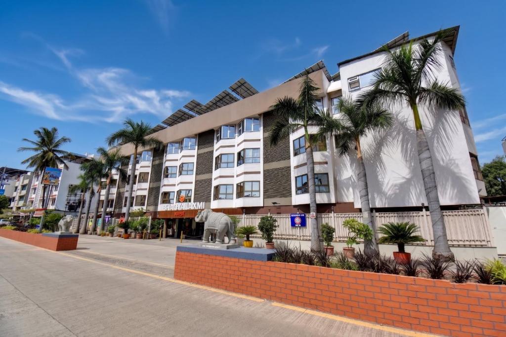 a building with palm trees in front of a street at Hotel Bhagyalaxmi in Shirdi