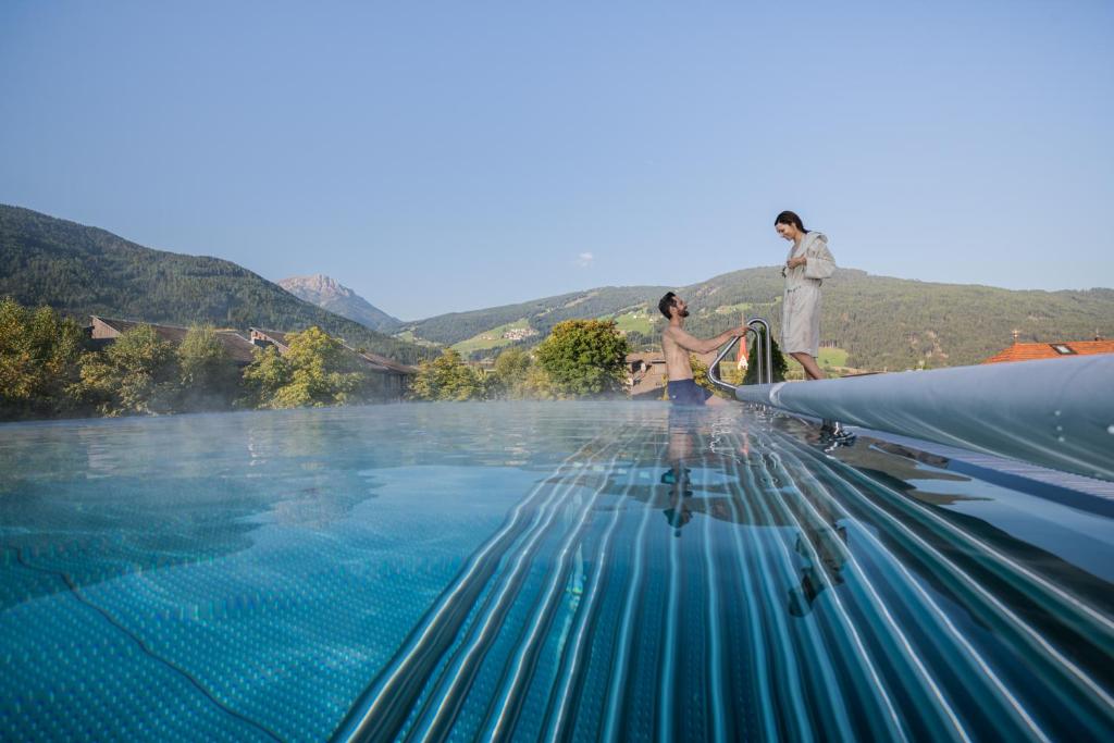 a group of people standing on the edge of a swimming pool at Hotel Fameli in Valdaora
