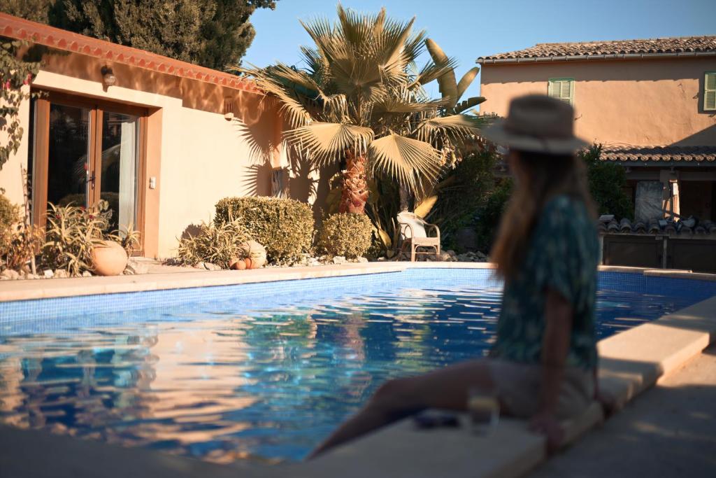 a woman in a hat sitting next to a swimming pool at Finca Caballo Blanco in Montuiri